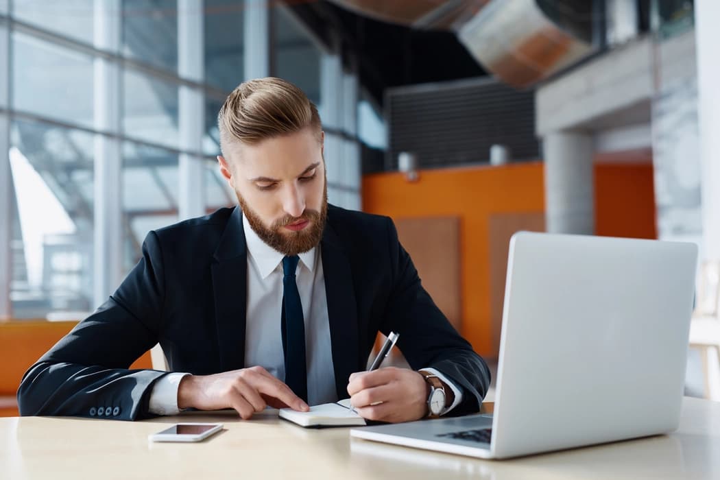 A candidate working through notes at a desk beside a laptop